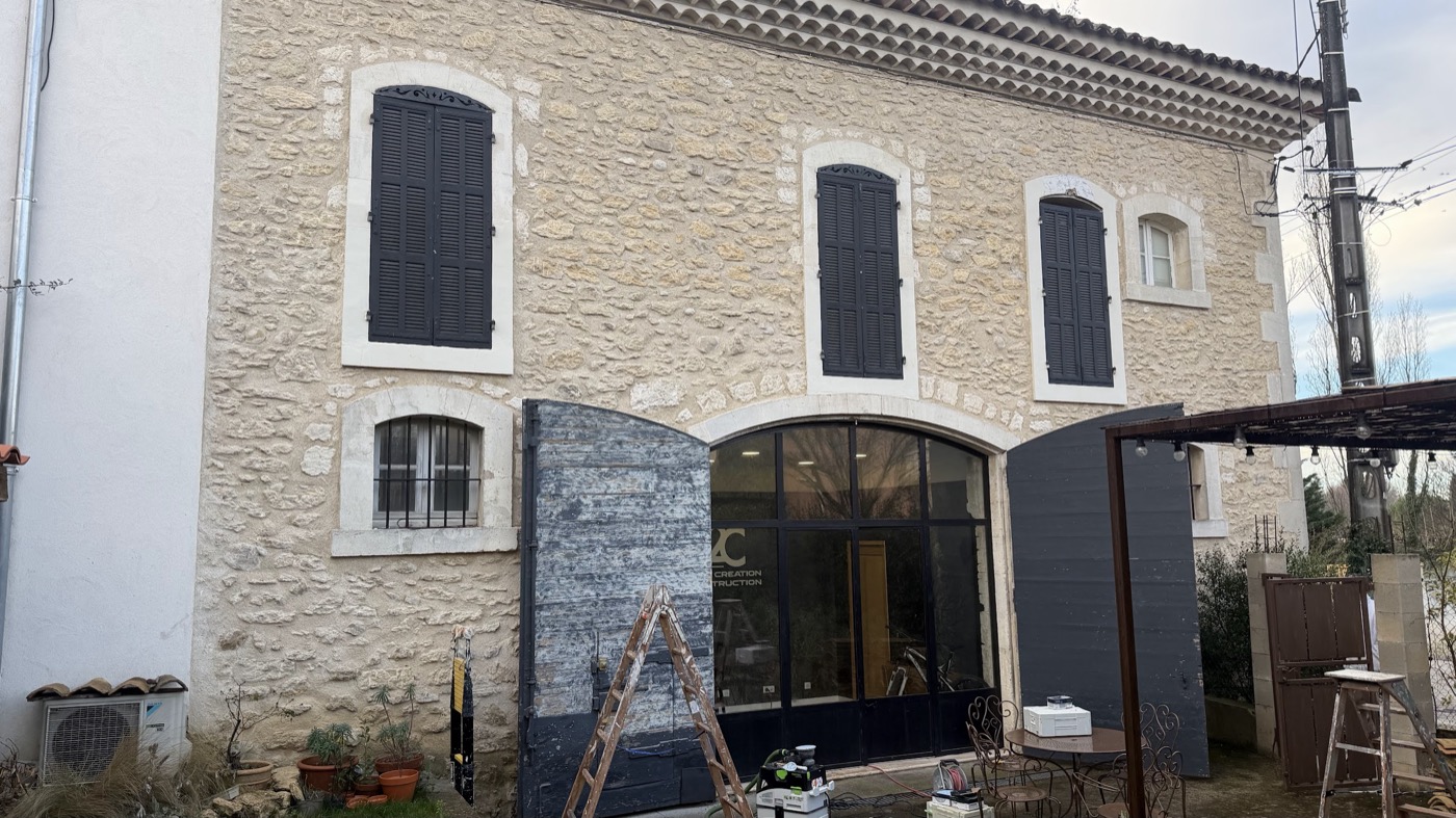 Façade de mas en pierre apparente, grande porte cochère et volets anthracite
